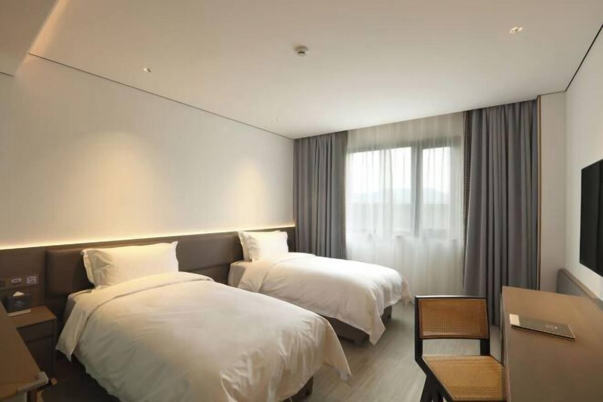 A hotel room with two beds, a desk, a chair, and a TV.