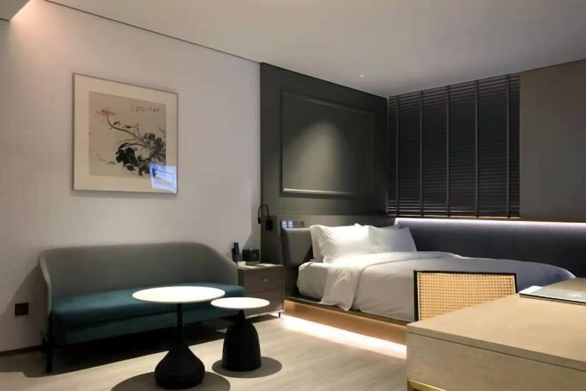 A modern hotel room with a bed, a sofa, a small table, and a nightstand.