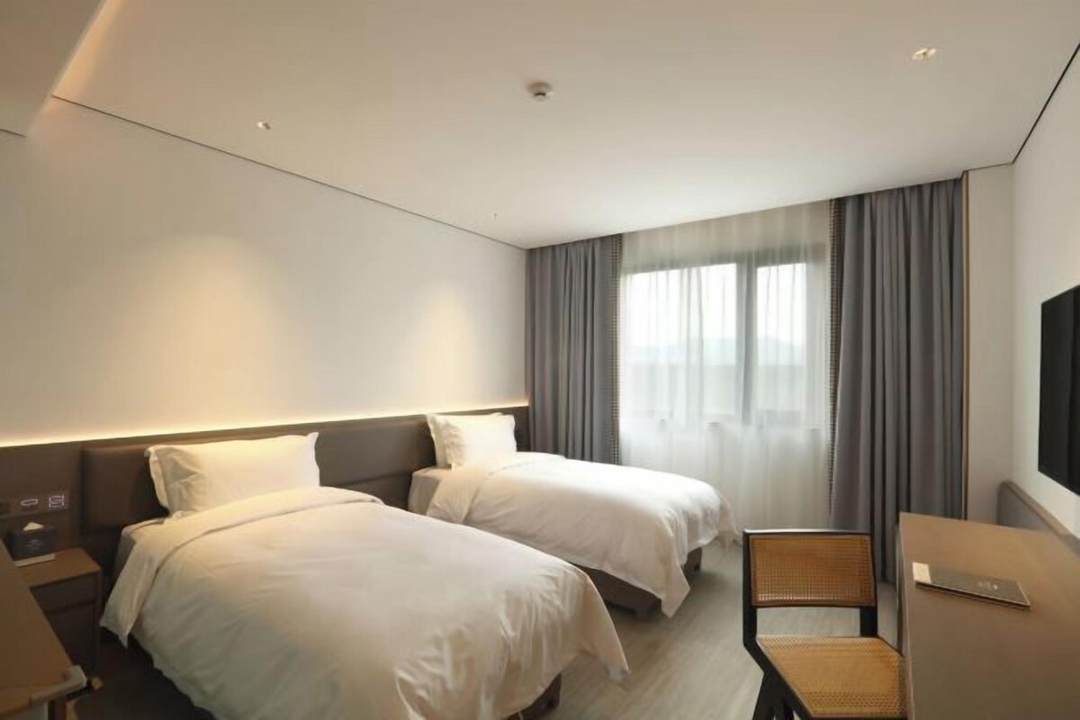 A hotel room with two beds, a desk, a chair, and a TV.