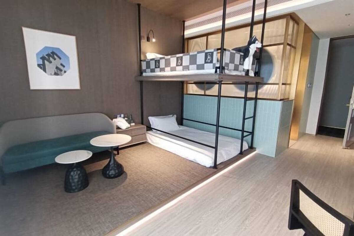 A room with a bunk bed, a sofa, two round tables, and a wall-mounted light fixture.