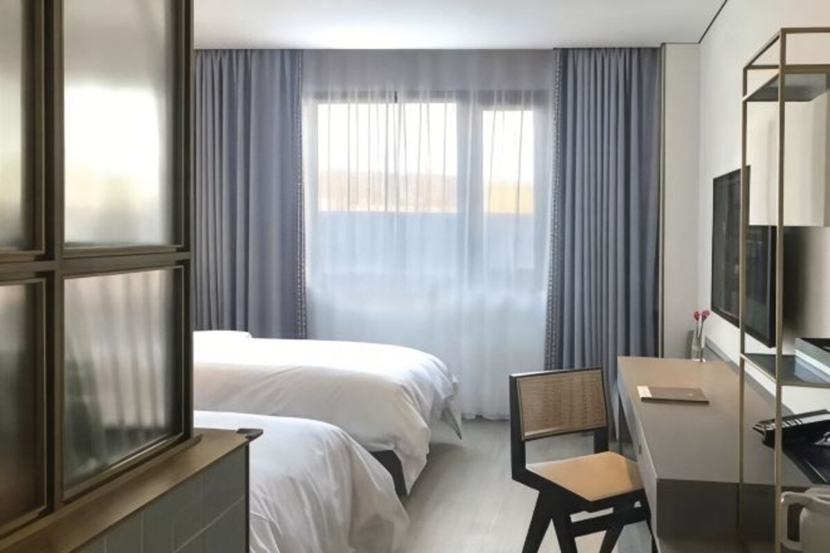 Habitación de hotel con dos camas, un escritorio, una silla, un televisor y una ventana con cortinas.
