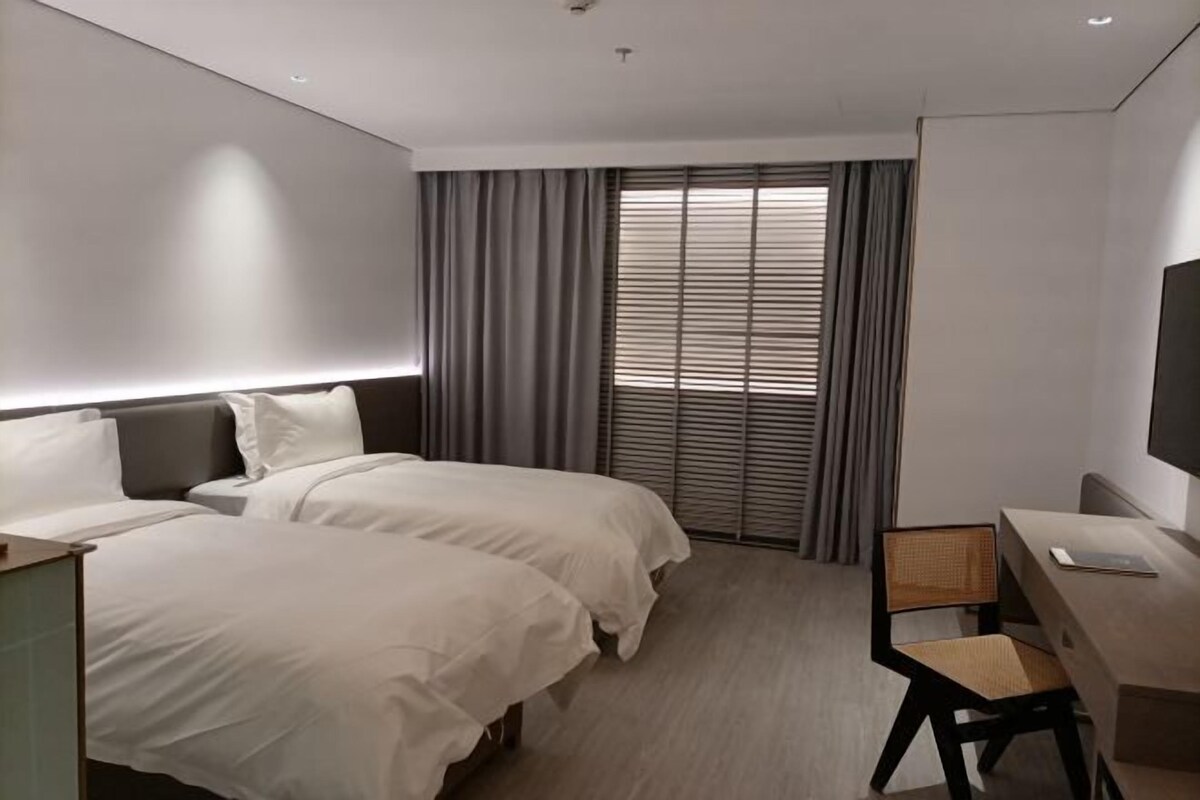 A hotel room with two beds, a desk, a chair, and a TV.