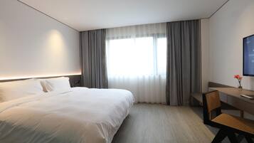 A hotel room with a large bed, a desk with a chair, a television, and a window with curtains.