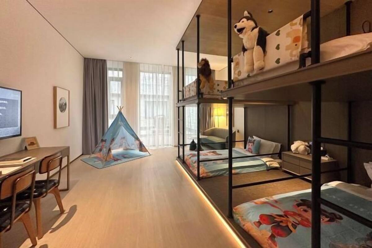 A modern hotel room with bunk beds, a desk, a chair, a laptop, and a tent.