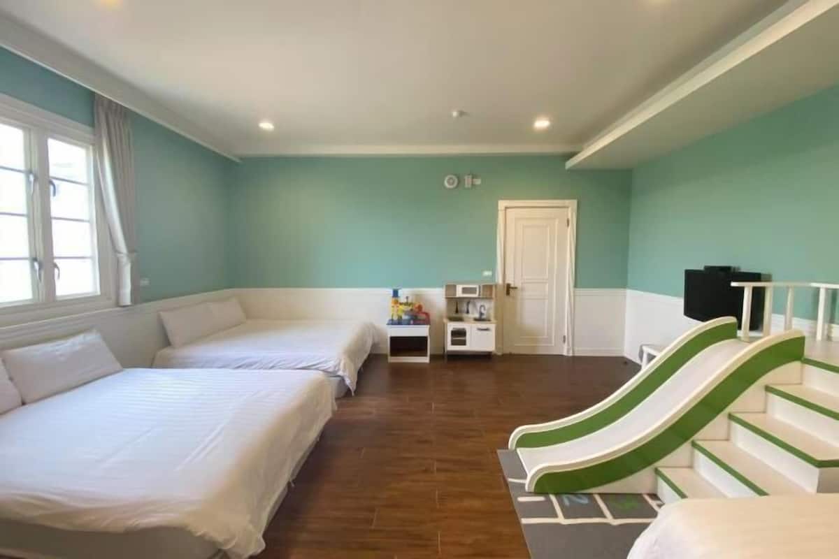 A room with two beds, a small kitchenette, a door, and a green and white slide.