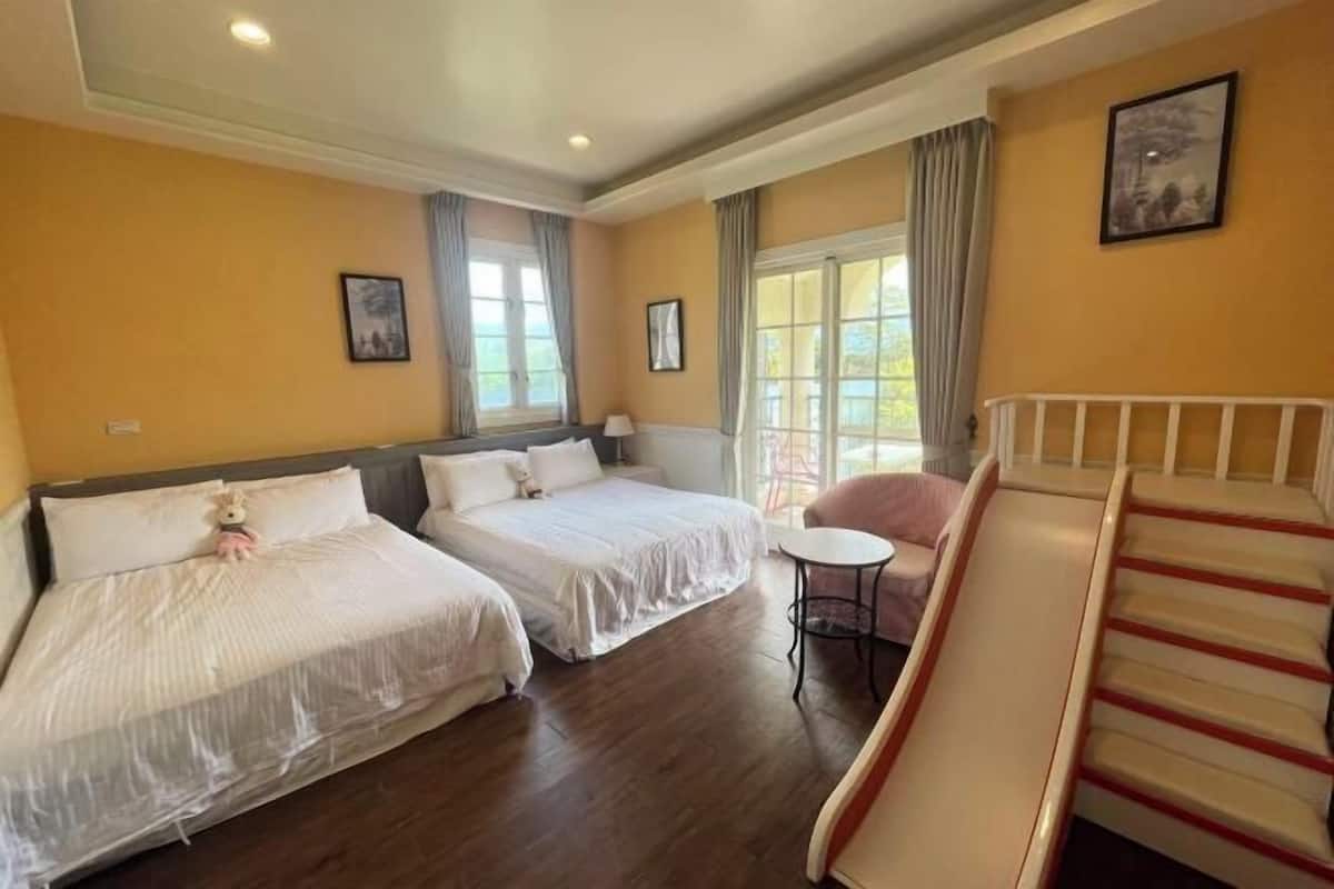 A hotel room with two beds, a small table, a chair, and a staircase.