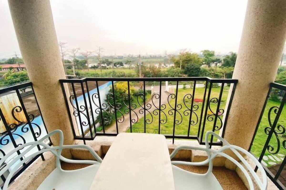 A balcony with a table and chairs, a view of greenery and distant buildings.