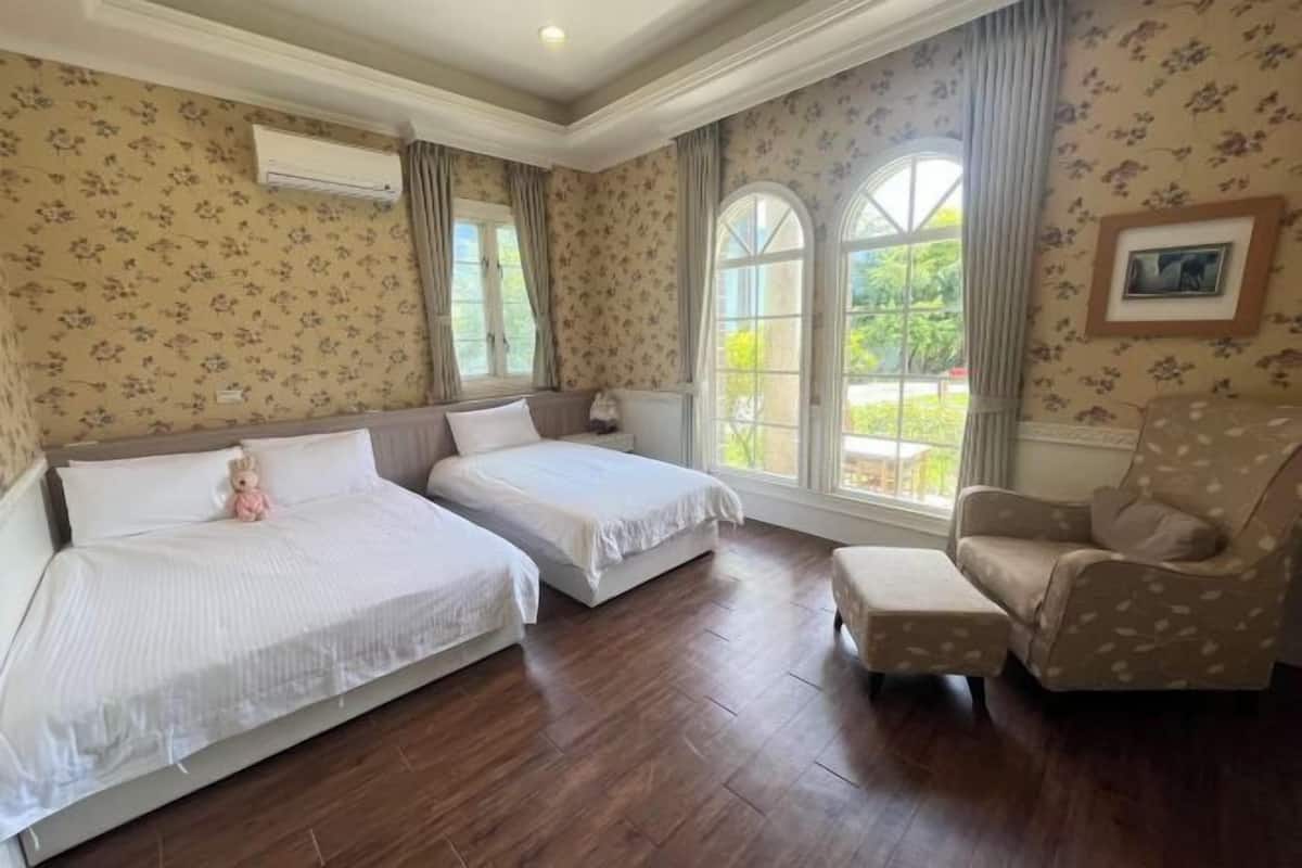 A room with two beds, a chair, and large windows.