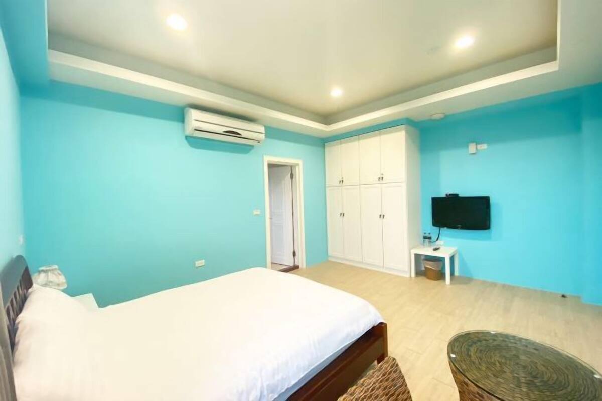 A bedroom with a bed, a wardrobe, an air conditioning unit, a television, and a small table.