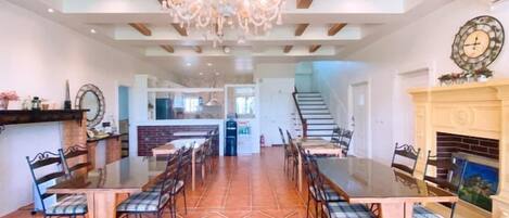 A spacious dining area with a long table and chairs, a chandelier, and a fireplace.