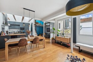 A modern kitchen with a dining area, wooden flooring, and a large window providing natural light. - Grandeur Cachée du 15e - avec parking (Paris)