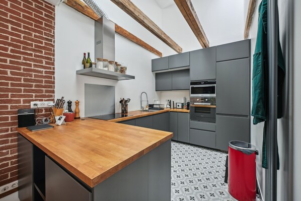 A modern kitchen with grey cabinets, a wooden countertop, and a brick wall. - Grandeur Cachée du 15e - avec parking (Paris)