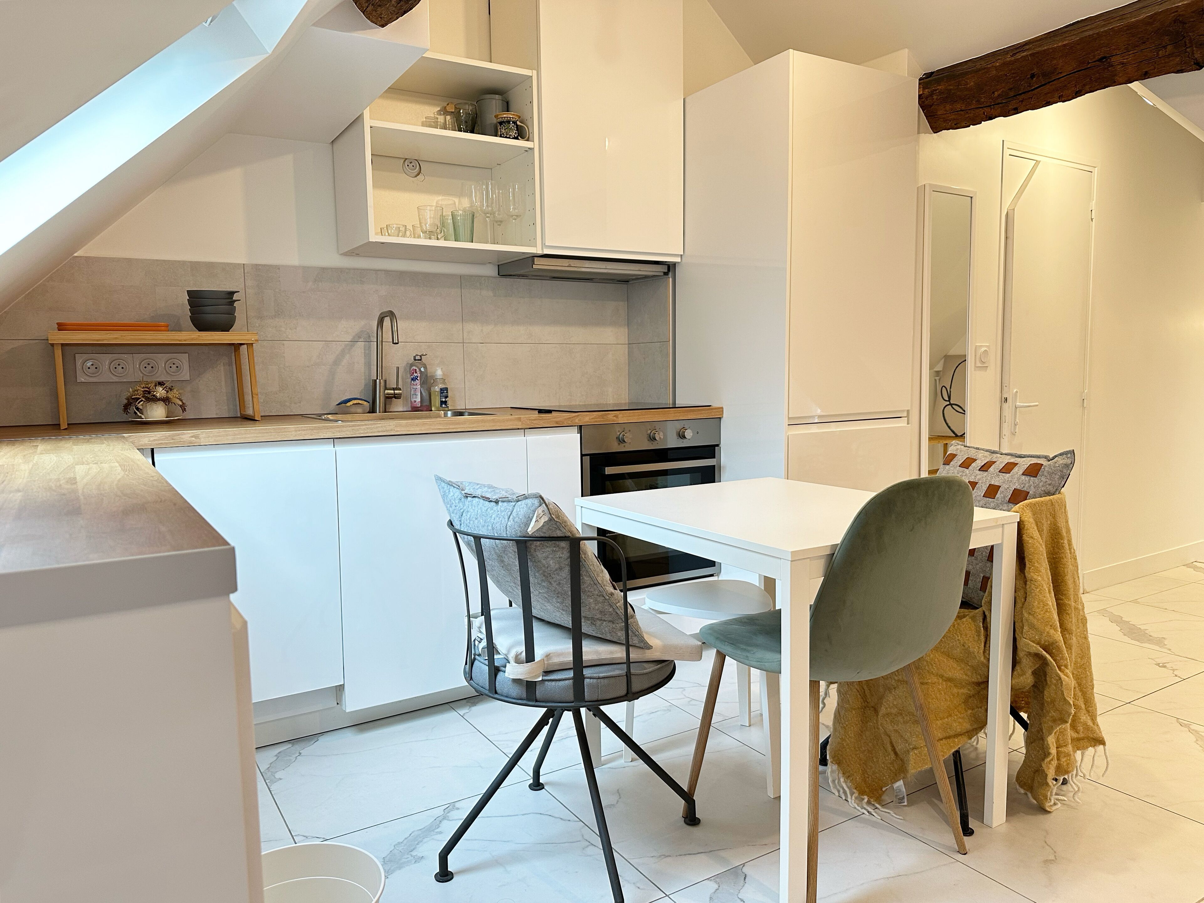 A modern kitchen with white cabinetry, a built-in oven, and a dining area with a table and chairs.