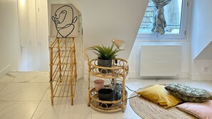 A modern loft bedroom with a sloped ceiling, a large window with patterned curtains, a rattan chair, a wall-mounted mirror, and a decorative plant. - Lovely Rooftop designed Apt 200m to Panthéon  (Paris)