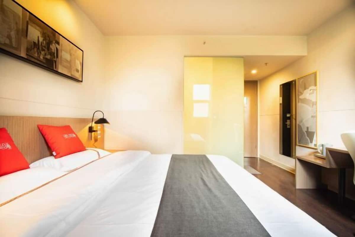 A hotel room with a bed, a desk, a chair, a lamp, and a painting on the wall.
