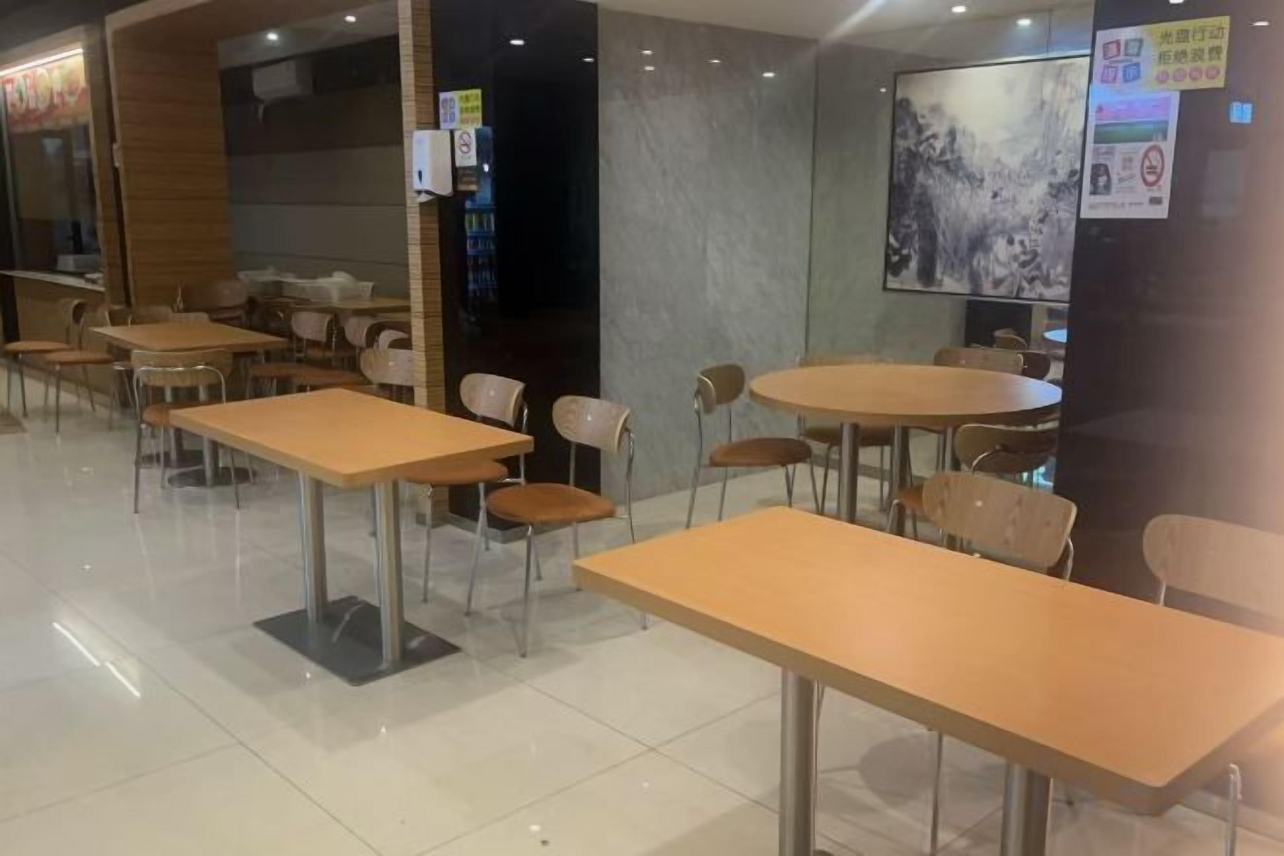 A restaurant with tables and chairs, a large painting on the wall, and a menu board.