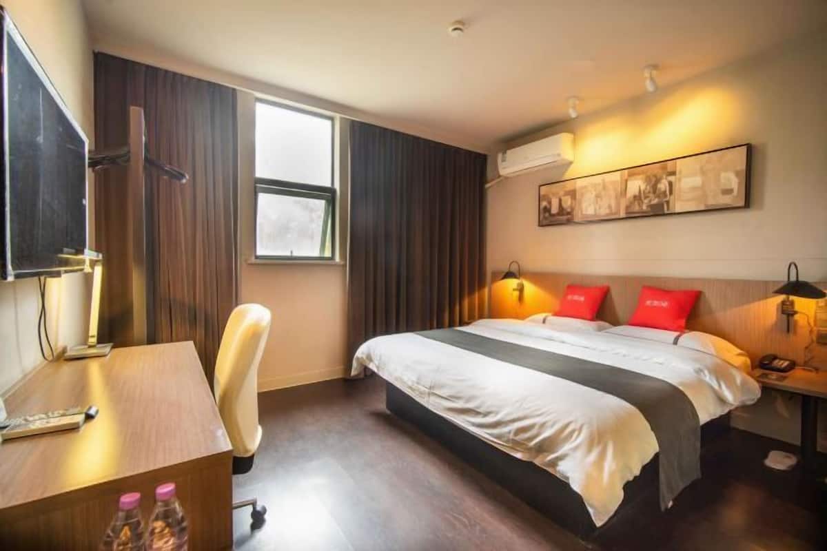 A hotel room with a bed, desk, chair, and artwork on the wall.