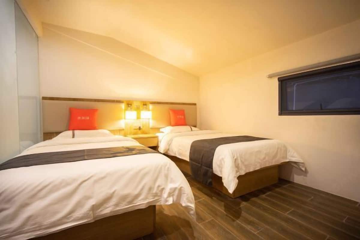 A hotel room with two beds, a nightstand with lamps, and a window.