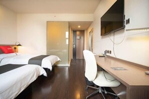 Hotellihuone, jossa on kaksi sänkyä, työpöytä, tuoli, televisio ja käytävä, joka johtaa toiseen huoneeseen.