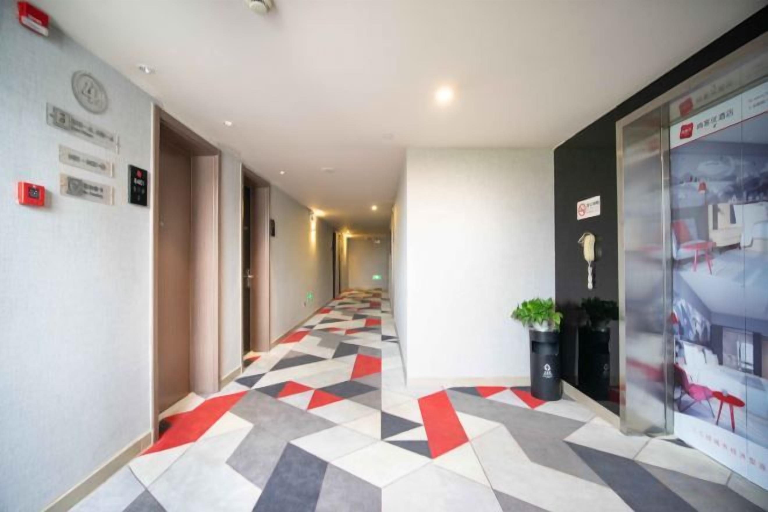 A hotel corridor with a geometric patterned floor, a clock, and a poster on the wall.