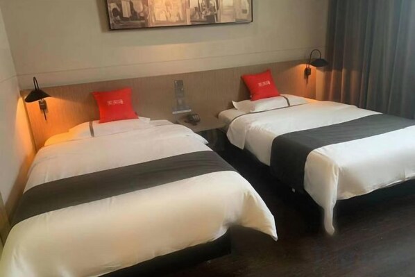 Two beds with white bedding and red pillows, a wall-mounted artwork, and a dark wooden floor.