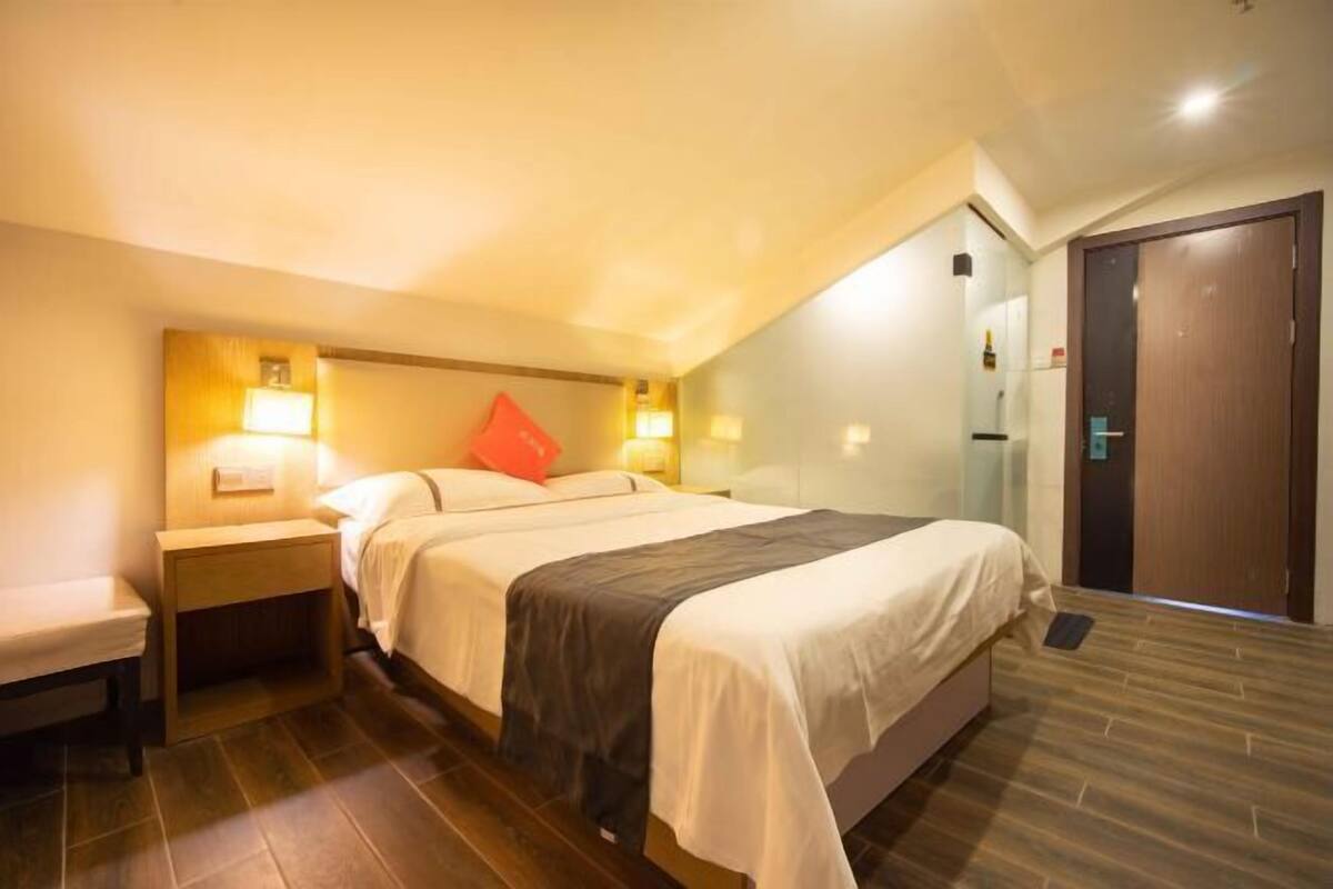 A hotel room with a bed, bedside tables, a bench, a mirror, and a door.