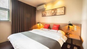 Ein Hotelzimmer mit einem großen Bett, zwei Nachttischen mit Lampen, einer Wand-Klimaanlage und einem gerahmten Bild über dem Bett.