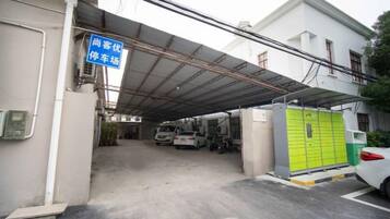 Un parking couvert avec une entrée abritée, un local de stockage vert et une voiture blanche garée à l’intérieur.