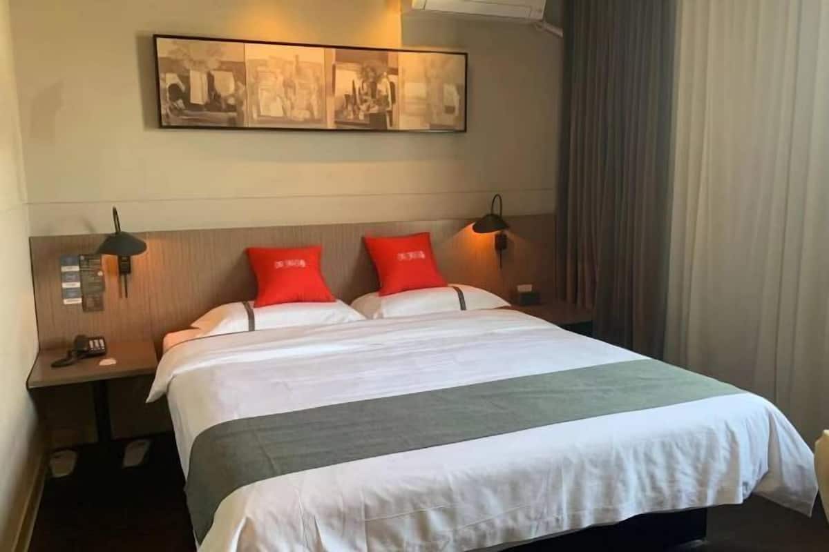 A hotel room with a bed, two nightstands, a wall-mounted artwork, and a window with curtains.