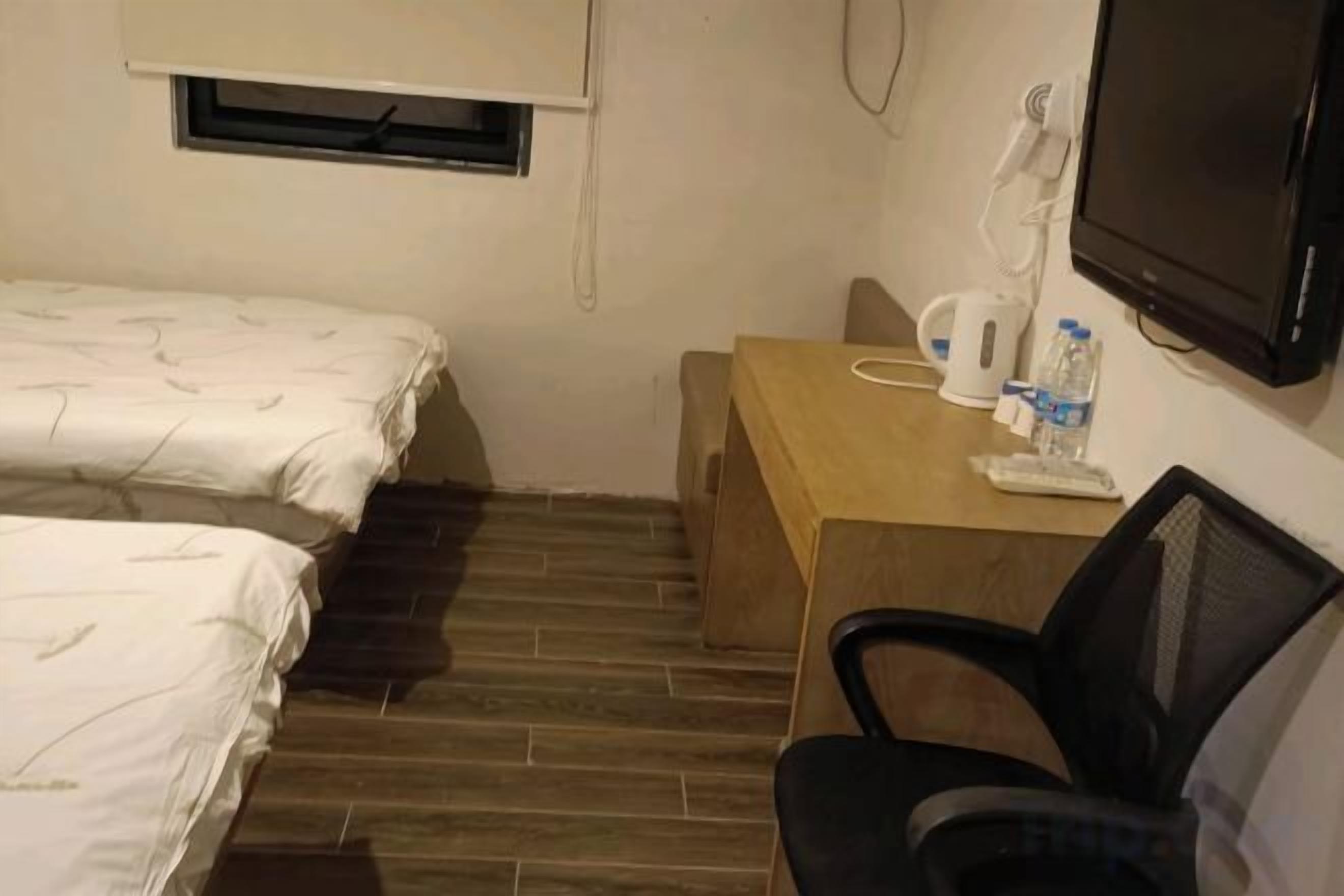 Habitació petita amb dos llits, un escriptori de fusta, una cadira, un televisor i una finestra.
