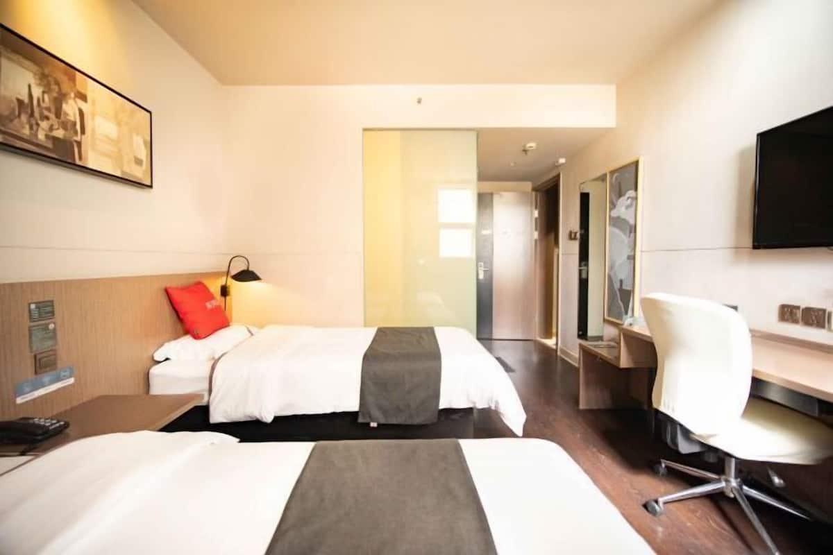 A hotel room with two beds, a desk, a chair, a TV, and a painting on the wall.