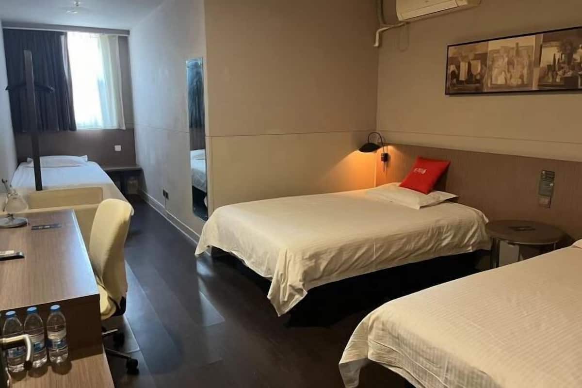 A hotel room with two beds, a desk with a chair, a small table, and a wall-mounted lamp.