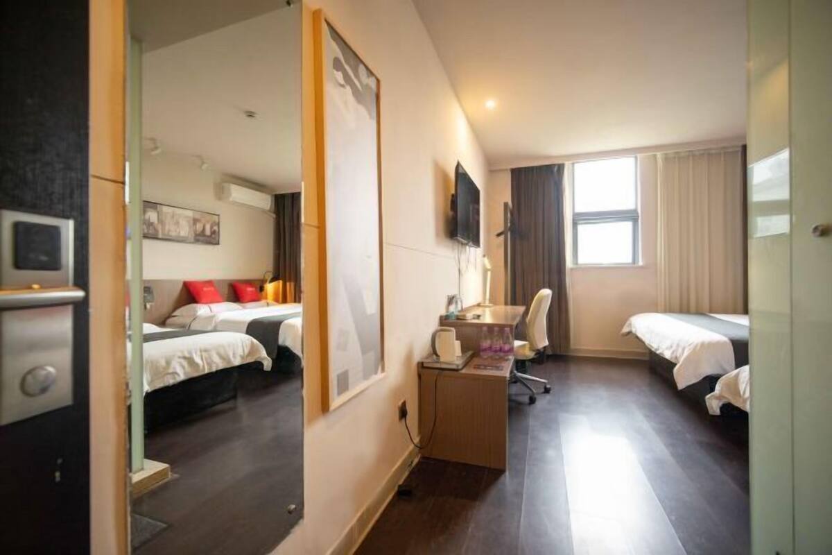 A hotel room with two beds, a desk, a chair, a TV, and a window.