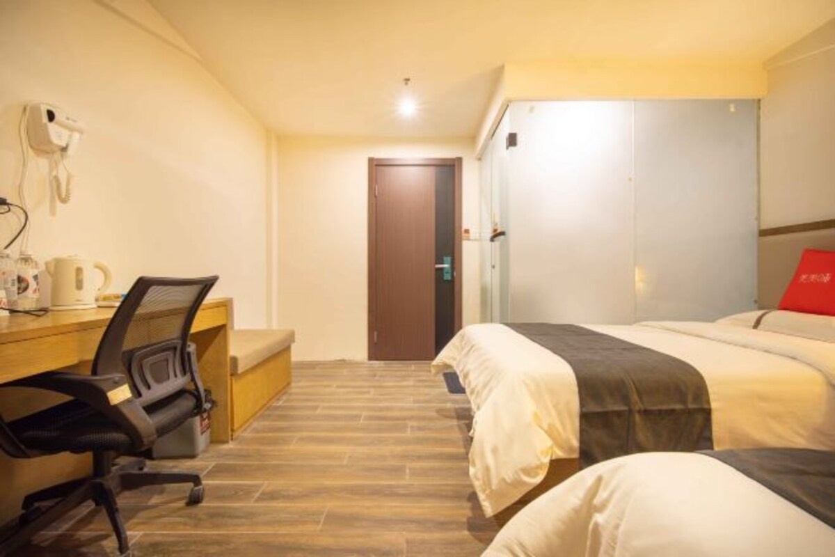 Hotellihuone, jossa on puinen työpöytä, tuoli, sänky, jossa on kaksi tyynyä, vaatekaappi ja ovi.