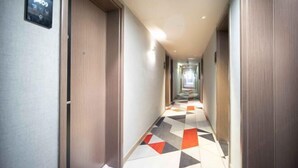 Ein Hotelkorridor mit einem gemusterten Boden, Holztüren und einer digitalen Anzeige an der Wand.