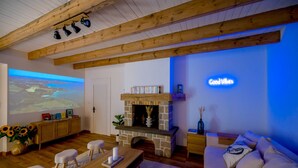 Ein gemütliches Wohnzimmer mit Kamin aus Stein, Holzbalken, einer Projektionsleinwand und einem Schild mit der Aufschrift 'Good Vibes'.
