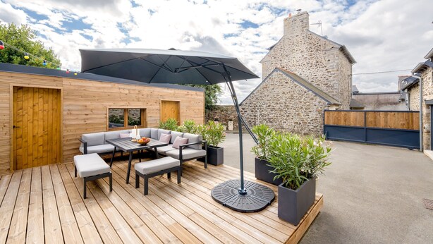 Eine Holzterrasse mit Essgruppe und einem großen Sonnenschirm.
