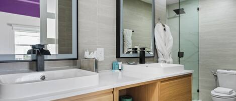 A modern bathroom with a large mirror, two sinks, a toilet, and a shower area.