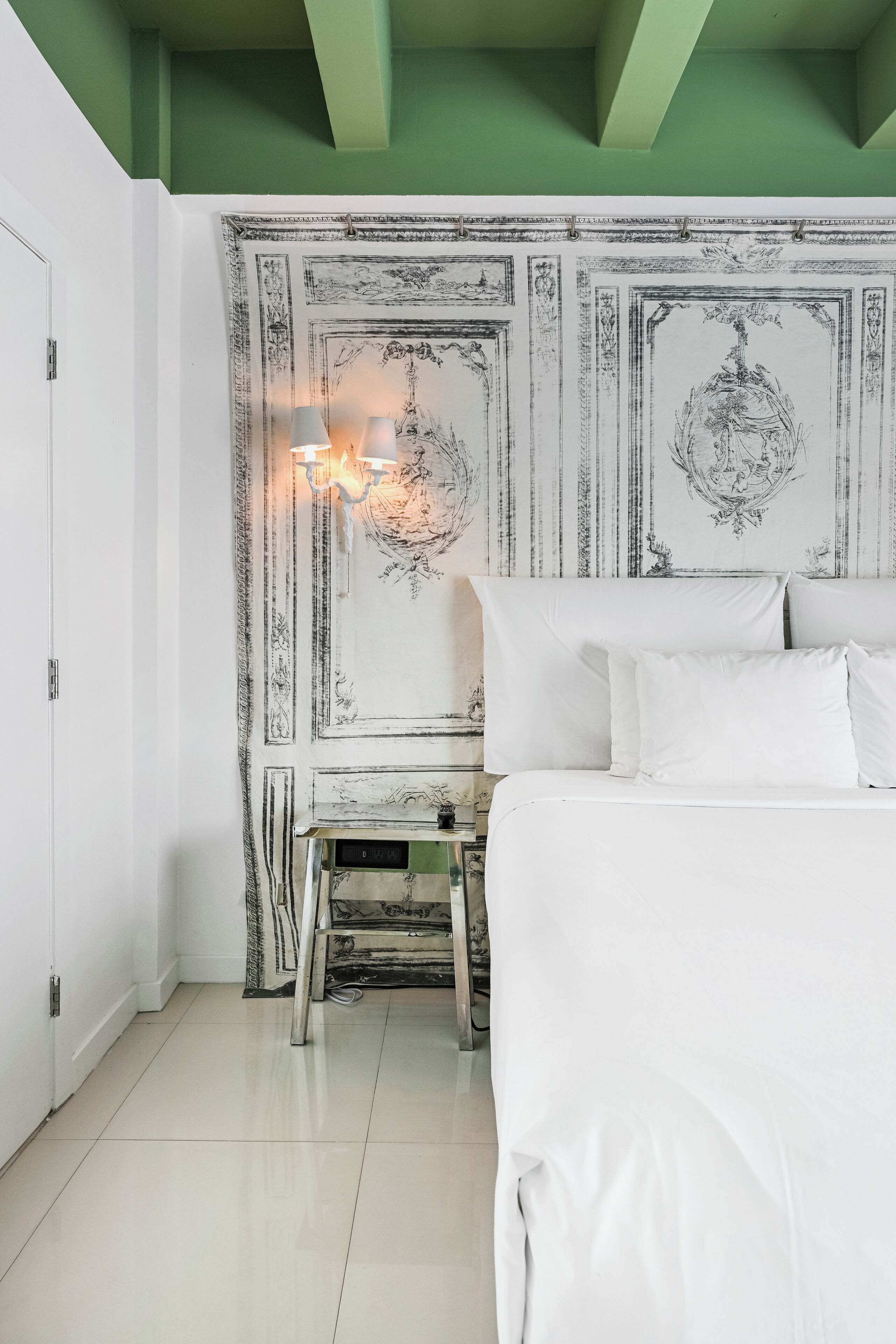 A bedroom with a bed, a nightstand, a wall with intricate designs, and a green ceiling.