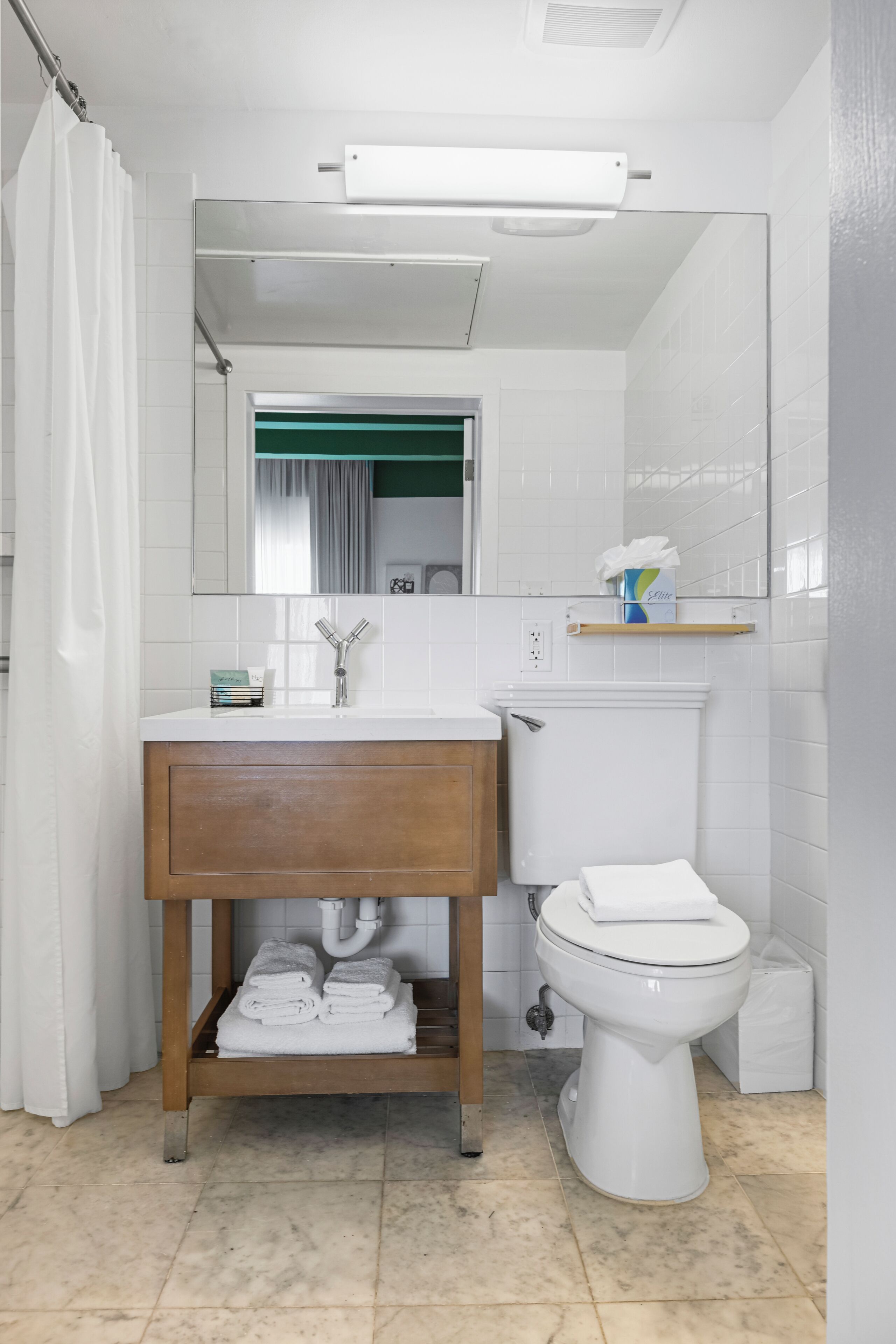 Un baño con lavamanos blanco, tocador de madera, inodoro y espejo.