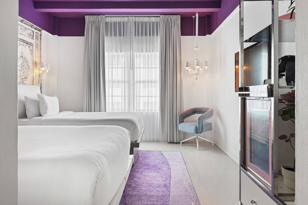 Moderni hotellihuone, jossa on sänky, tuoli, peilipöyt ä ja suuri ikkuna, jossa on verhot.