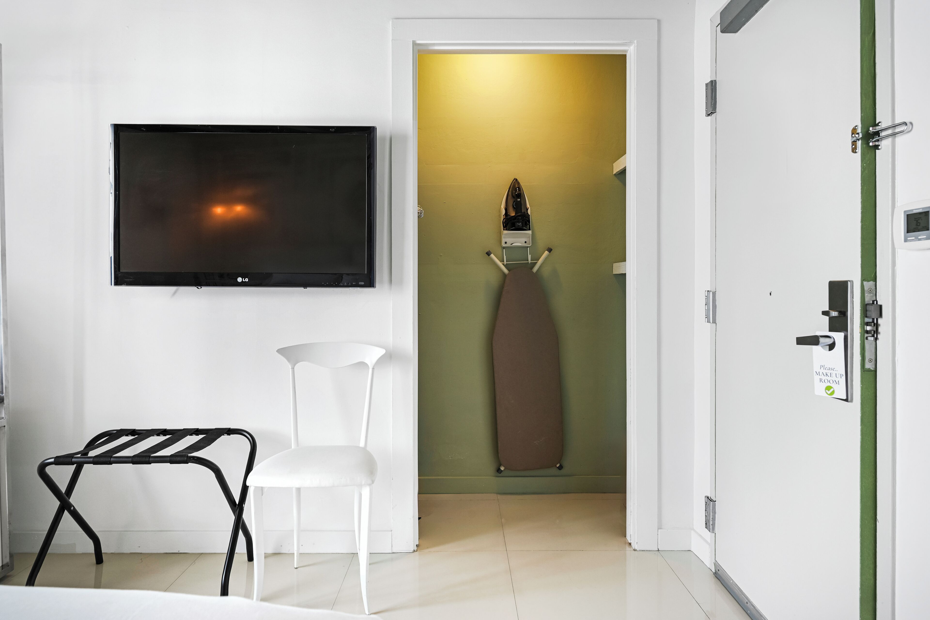 Ein Zimmer mit Flachbildfernseher, einem weißen Sessel, einem braunen Bügelbrett und einer Tür mit dem Schild 'Bitte Zimmer machen lassen'.