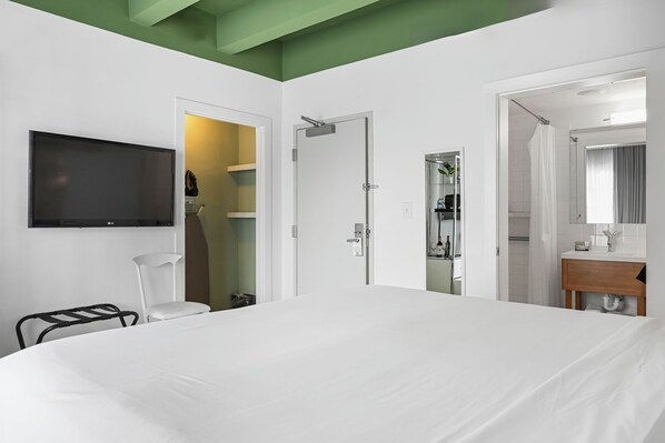 A hotel room with a bed, a TV, a shower, and a bathroom with a mirror.