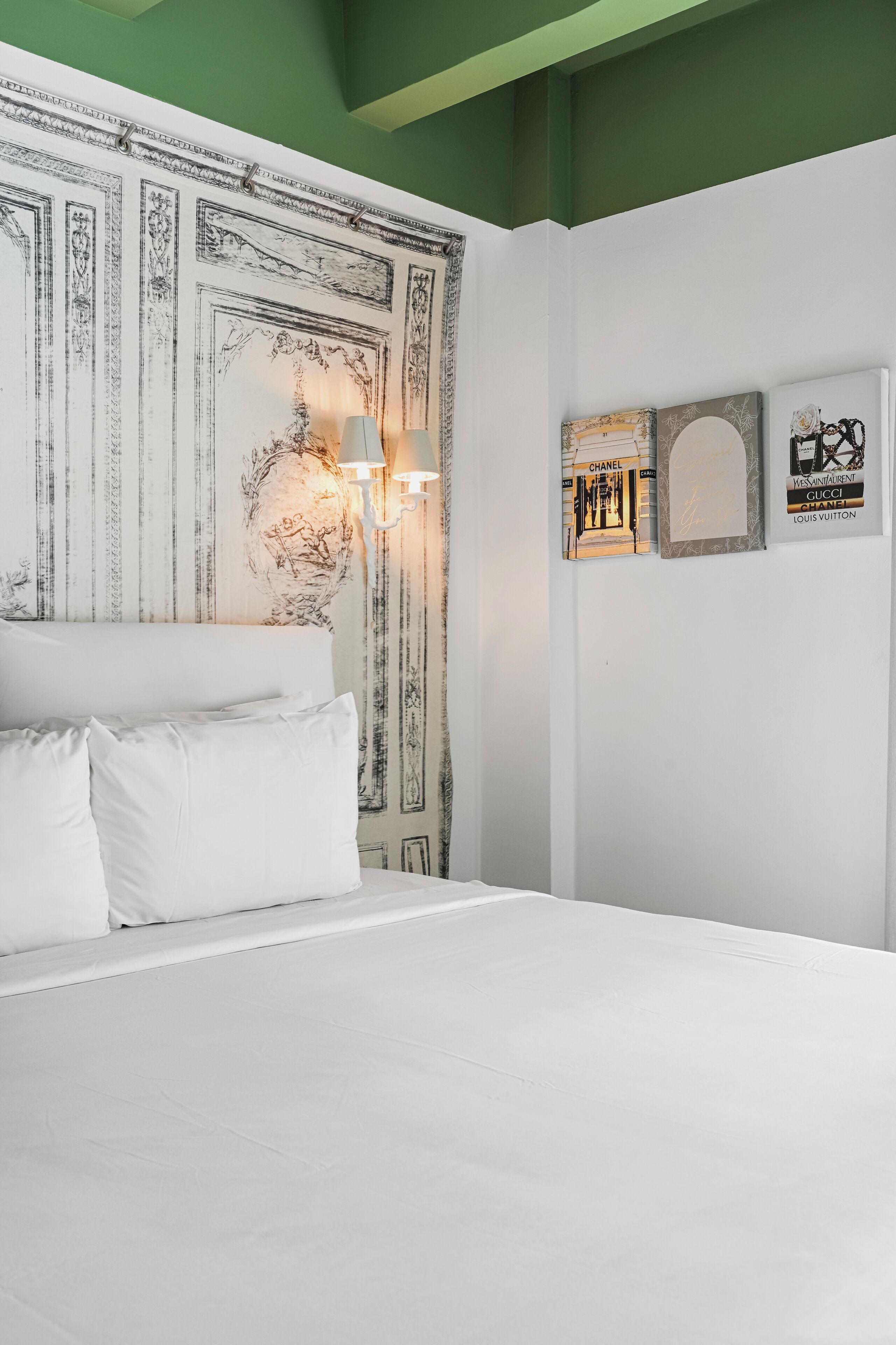 A hotel room with a large bed, a decorative headboard, a wall with framed artwork, and a green accent wall.