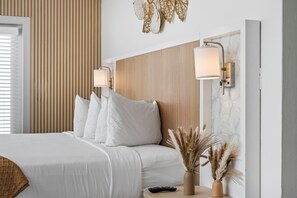 Habitación de hotel con cama, dos lámparas de pared, un florero con plantas secas y un control remoto sobre la mesita de noche.