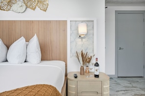 Una habitación de hotel con cabecera de madera, una mesita de noche con una botella de vino, un control remoto y una lámpara de pared.
