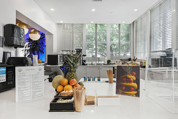 A modern cafe with a menu board, fruit display, and kitchen area. - Townhouse Hotel (Miami Beach)