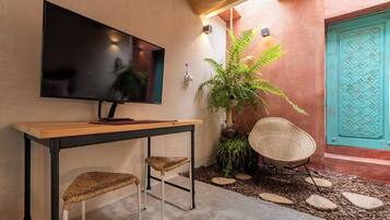 Ein modernes Interieur mit einem an der Wand befestigten Flachbildfernseher, einem Holztisch mit zwei gewebten Stühlen, einer Topfpflanze und einer türkisblauen Tür.