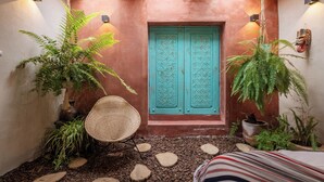 Una entrada acogedora con una puerta turquesa, plantas en macetas y un sillón de mimbre.