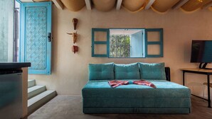 Un dormitorio con un sofá azul turquesa, un televisor y una ventana con contraventanas azules.